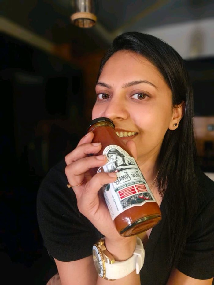 Garima Khandelwal, founder of The True Tomato, smiling with a bottle of her ketchup